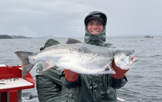 Alaska Fishing Report: A young angler smiles while he holds a large silver salmon aboard a fishing charter near Craig, AK.