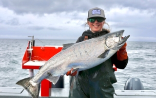 Alaska Fishing Vacation: An angler smiles as she holds a large silver salmon aboard a Screamin' Reels fishing boat near Craig, Alaska.