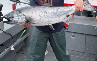 Avid angler smiles aboard a boat as she holds a large king salmon.